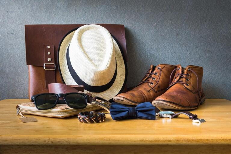 Men's casual wear on wooden table on grunge background wall (leather briefcase, watch, belt, bracelet, hat, shoes)