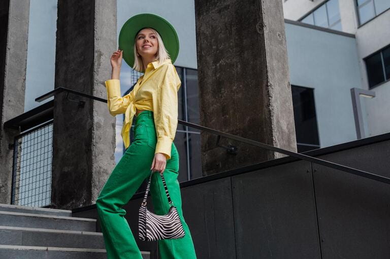 Street style, fashion portrait of happy smiling fashionable woman wearing green hat, wide leg jeans, yellow shirt, holding trendy zebra print, walking in city. Copy, empty space for text